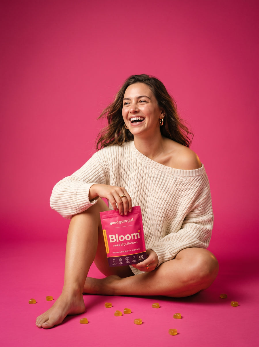 a woman laughing on a pink studio floor, holding the bloom pouch