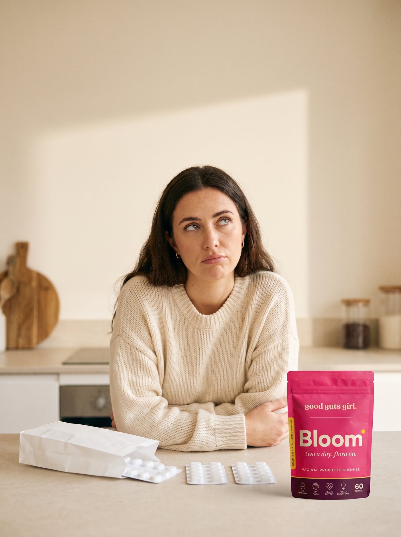 a woman at her kitchen counter, arms crossed, looking at another course of pills